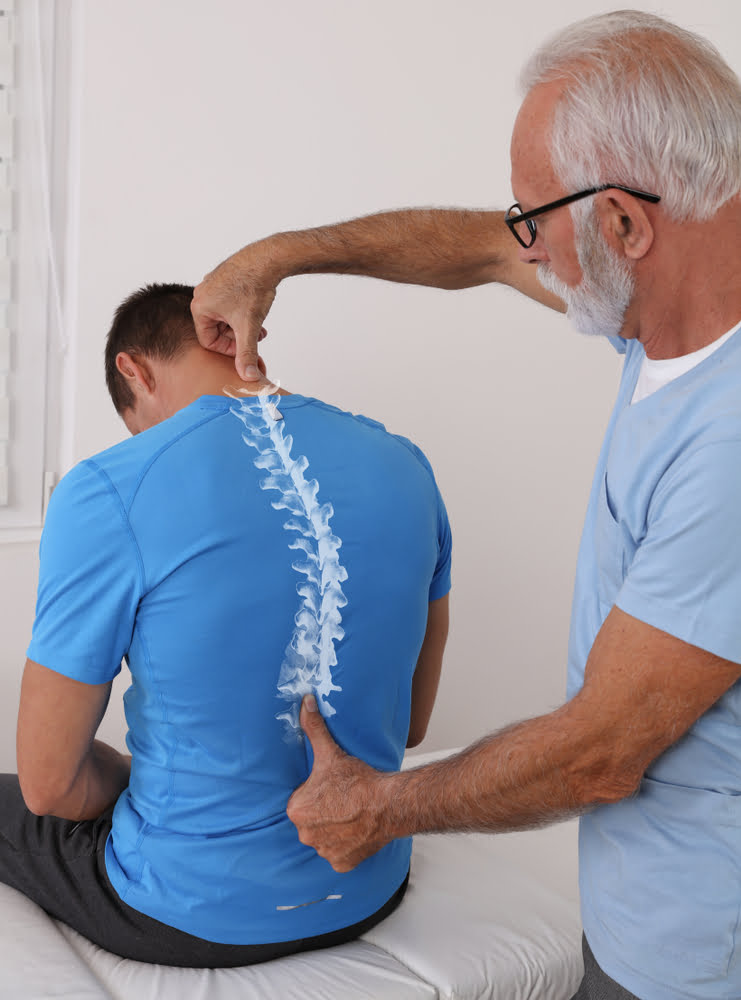 A chiropractor explaining spinal alignment to a patient using a spine model while pointing to the patient's back - Chiropractor Brunswick GA A chiropractor explaining spinal alignment to a patient using a spine model while pointing to the patient's back - Chiropractor Brunswick GA