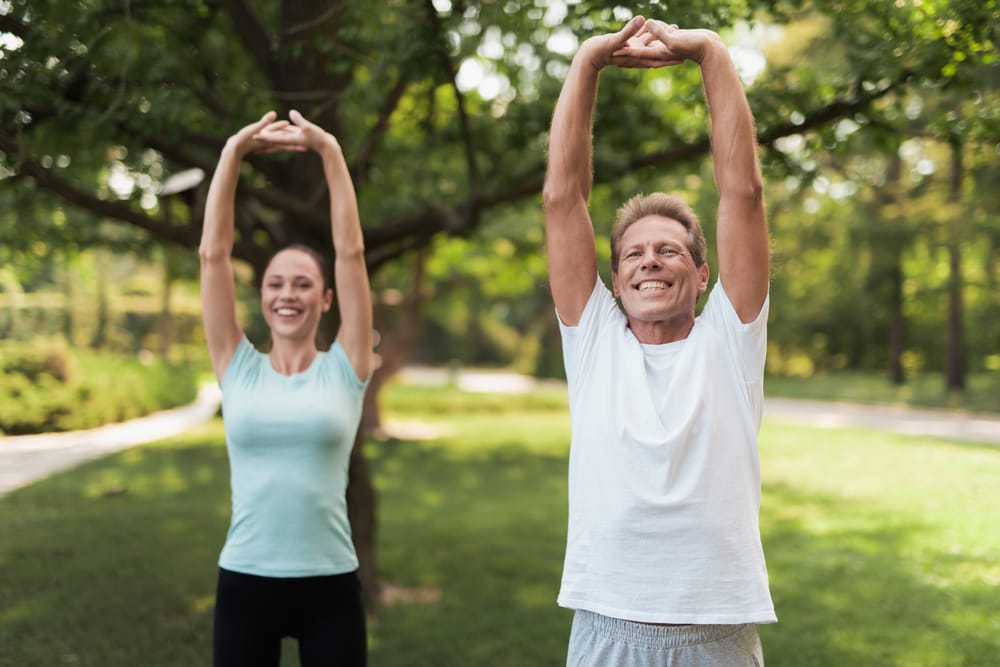 Two adults stretch outdoors as part of a healthy lifestyle routine that supports spinal flexibility, posture, and long-term mobility – Waynesville Chiropractor